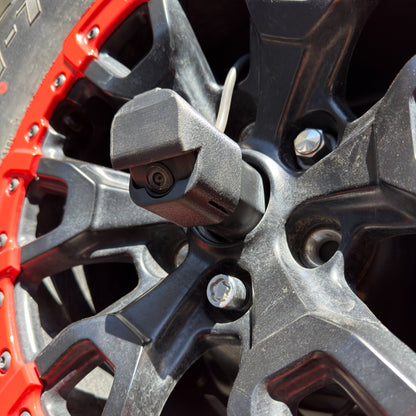 LensJet OEM nozzle housing installed on a Ford Bronco rear camera, mounted on a black and red Bronco Raptor spare tire wheel with the camera lens and spray nozzle visible between the spokes.