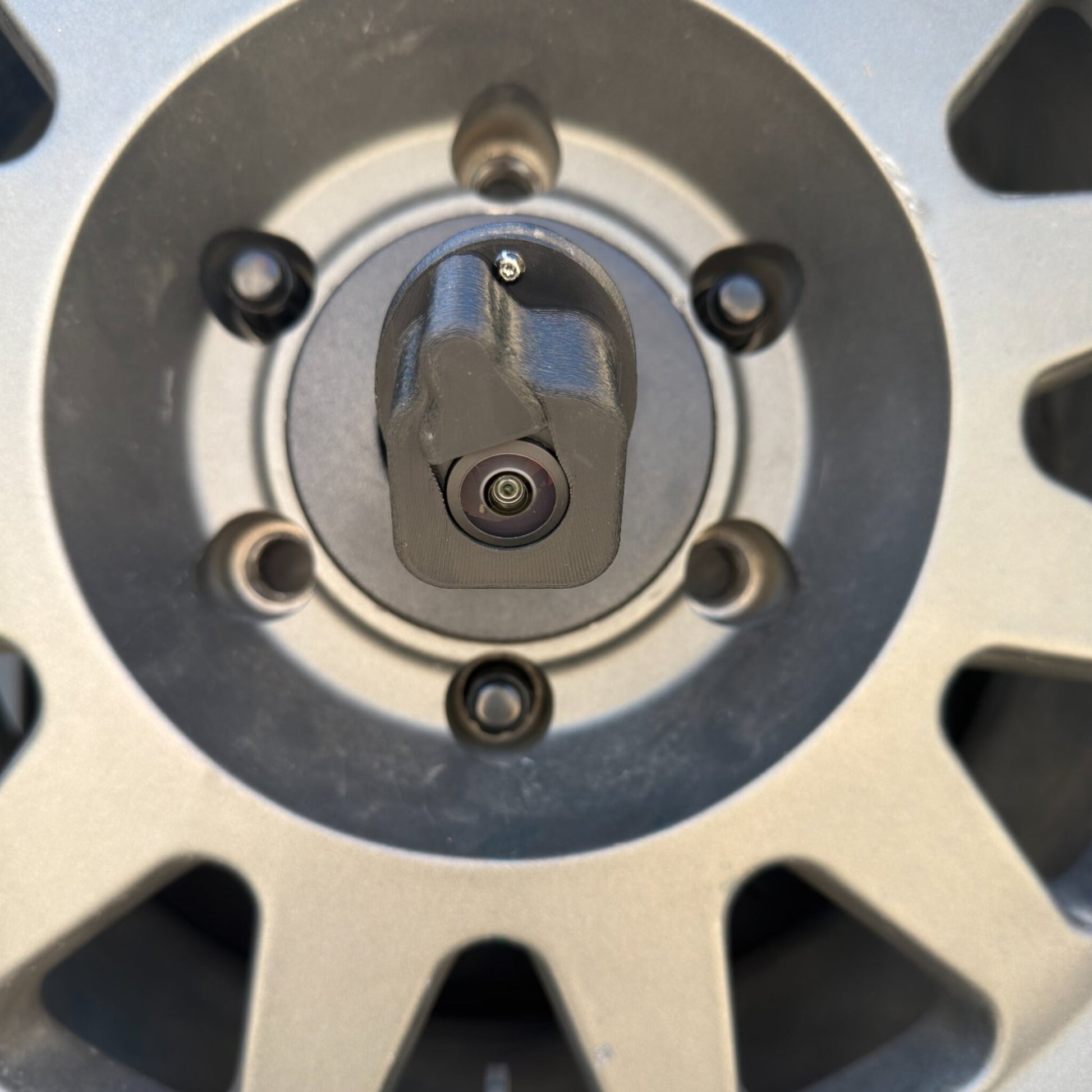 LensJet Turn Offroad nozzle housing installed on a Ford Bronco rear camera, centered in front of the spare tire wheel hub with the camera lens and spray nozzle visible between the lug bolt ring.