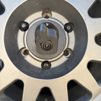LensJet Turn Offroad nozzle housing installed on a Ford Bronco rear camera, centered in front of the spare tire wheel hub with the camera lens and spray nozzle visible between the lug bolt ring.