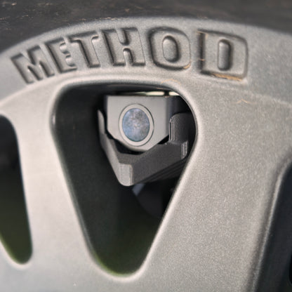 Close-up of the LensJet for Wolfbox mounting bracket and hardware framed by a Method wheel spoke